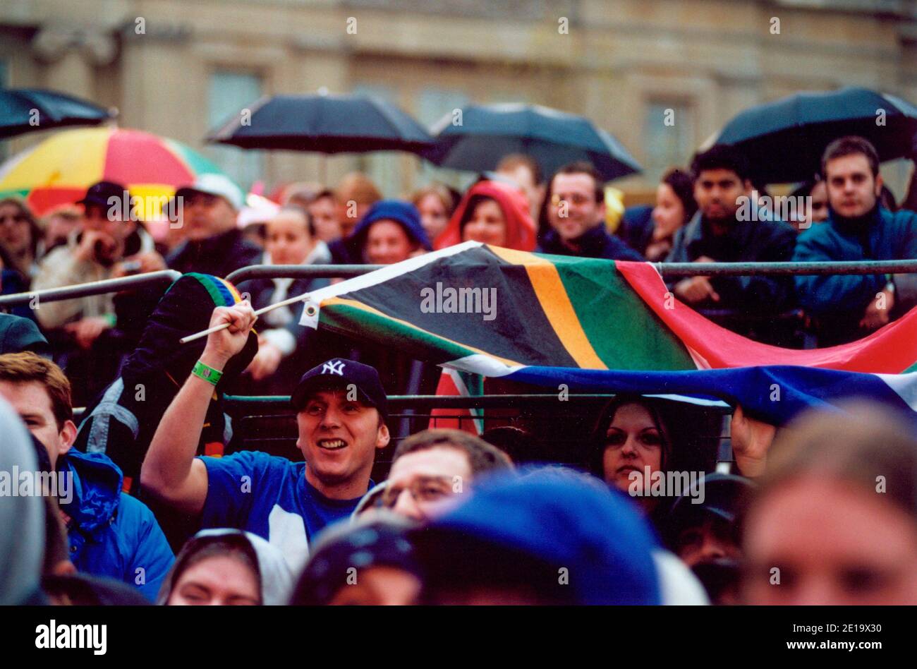 South African music fans use South African national flag to shelter from rain at Celebrate South Africa Freedom Day Concert, Trafalgar Square, London. Stock Photo