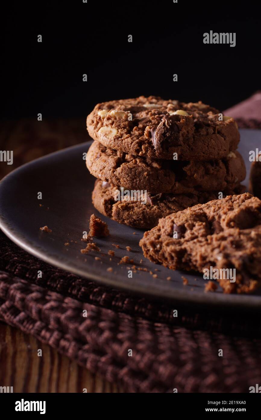 Triple chocolate chip cookies with chunks of white milk and dark chocolate shot with dark creative lighting Stock Photo