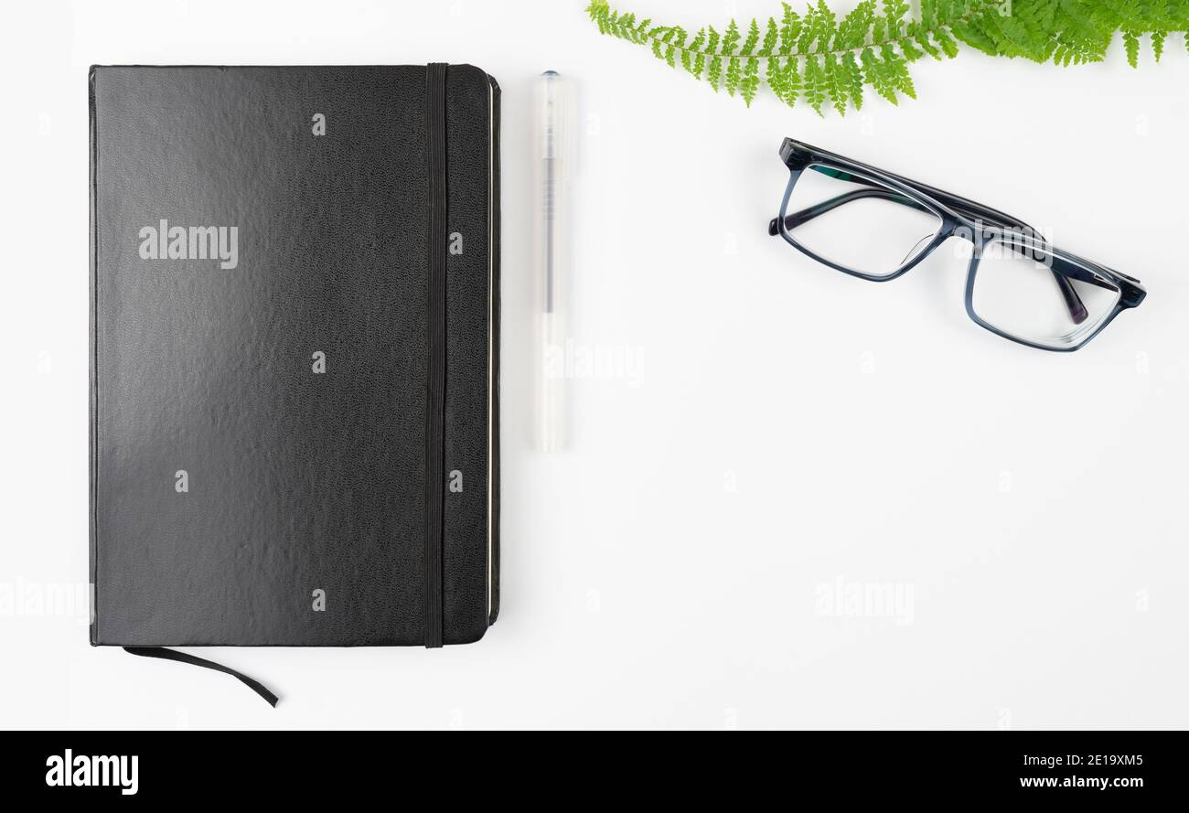 black notebook, pen and glasses on white table background with copy space Stock Photo