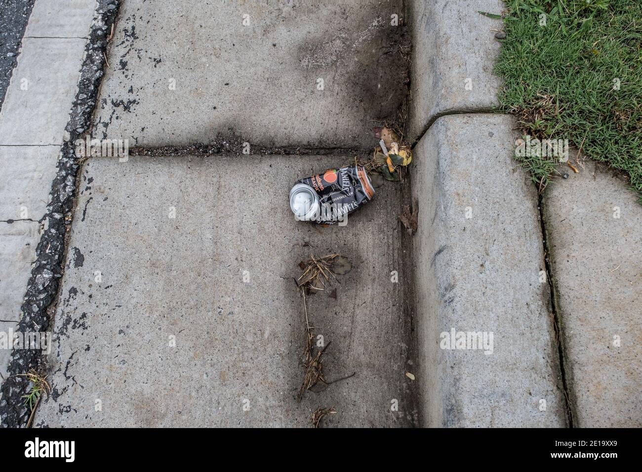 Discarded Jack Daniel's can crushed and thrown aside laying on the cement curb alongside the road polluting the environment Stock Photo