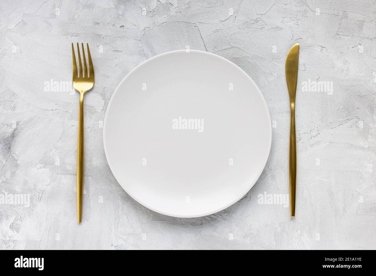 Golden cutlery and empty plate on gray background Stock Photo