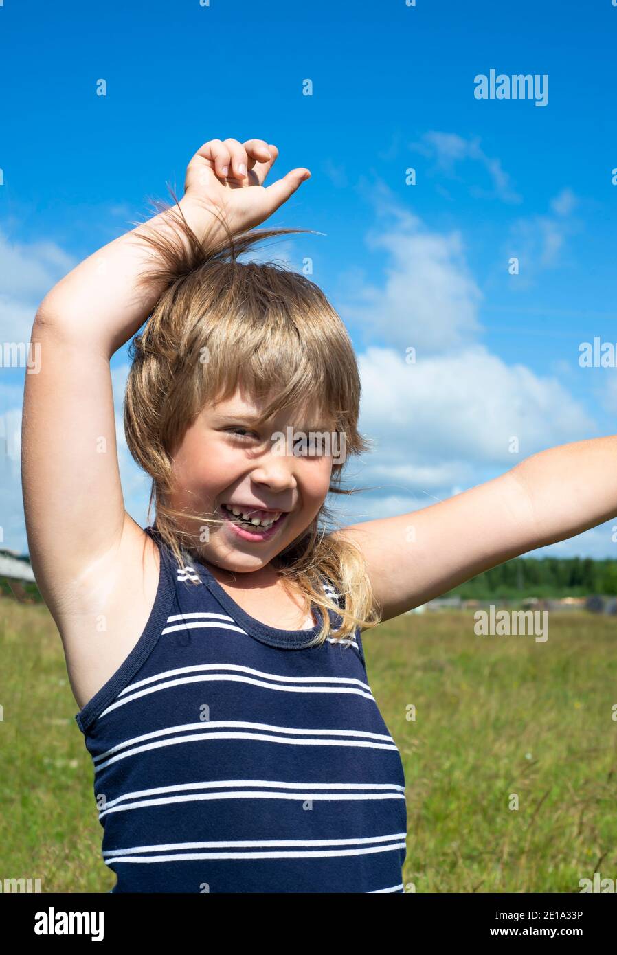 The boy is dancing and having fun in nature on the green grass. Overwhelmed with feelings of joy and happiness. Children's emotions are positive. Stock Photo