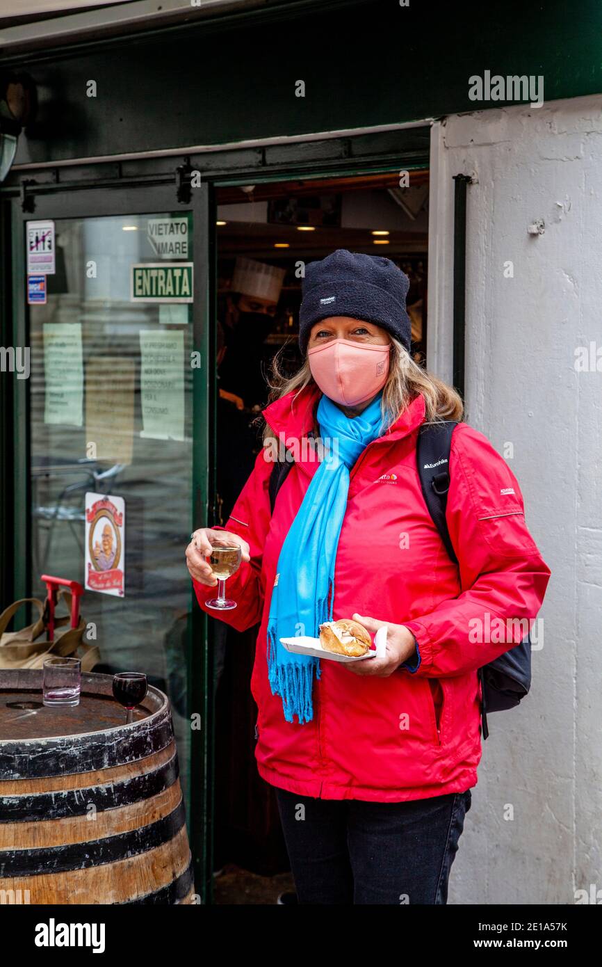 A Female Tourist Wearing A Face Mask Outside A Cafe With A Glass Of Wine and Sandwich During The Covid 19 Pandemic, Venice, Italy. Stock Photo