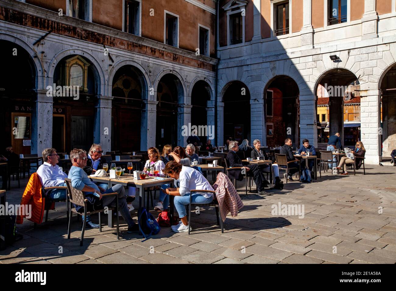 Tourists/Visitors Relaxing In The Sunshine At A Cafe Near The Rialto Bridge, Venice, Italy. Stock Photo