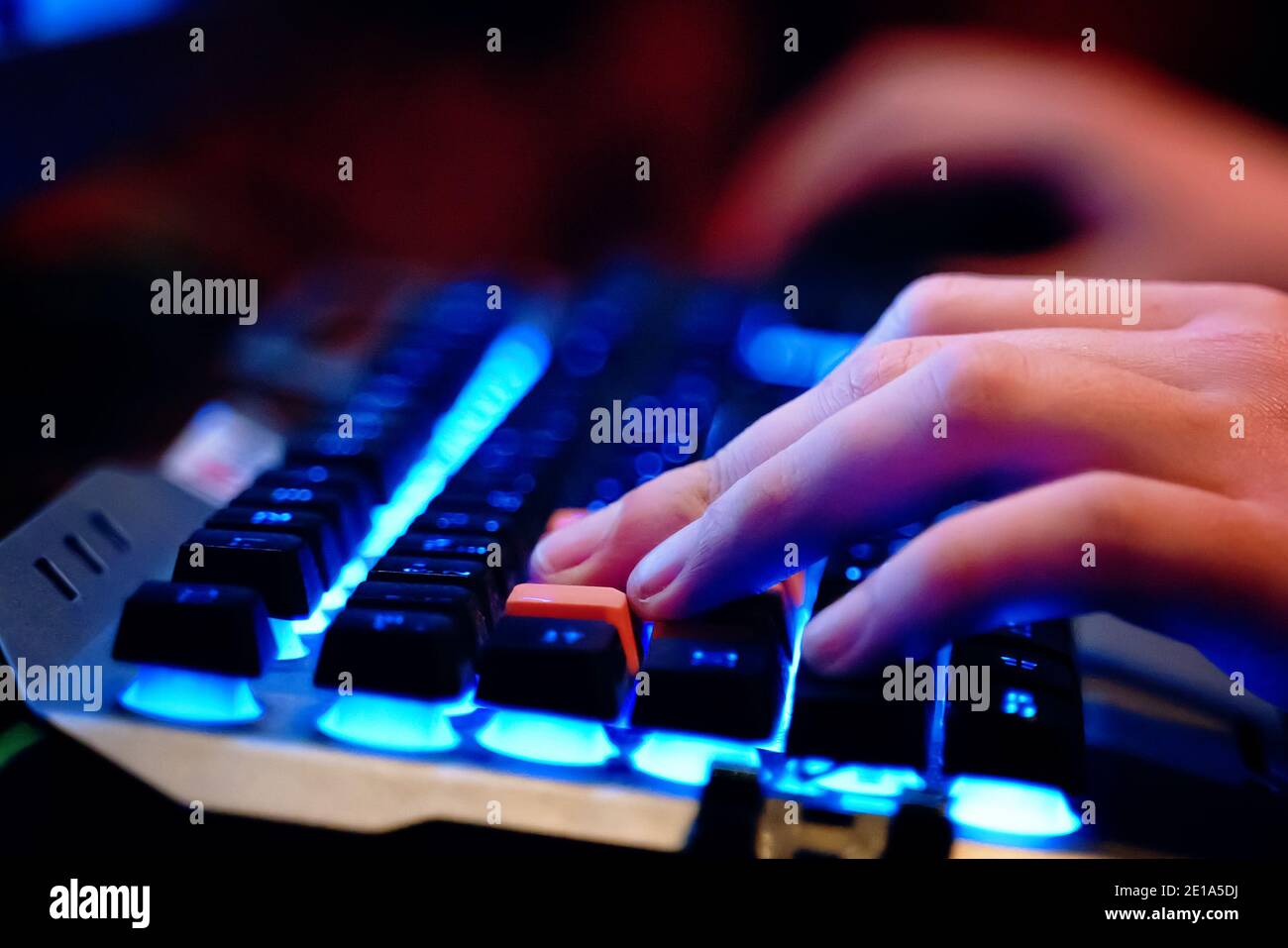 Close-up on human hands on a neon lit keyboard. Multifunction keyboard with set of red button. WASD keys are used in many video games.  Stock Photo