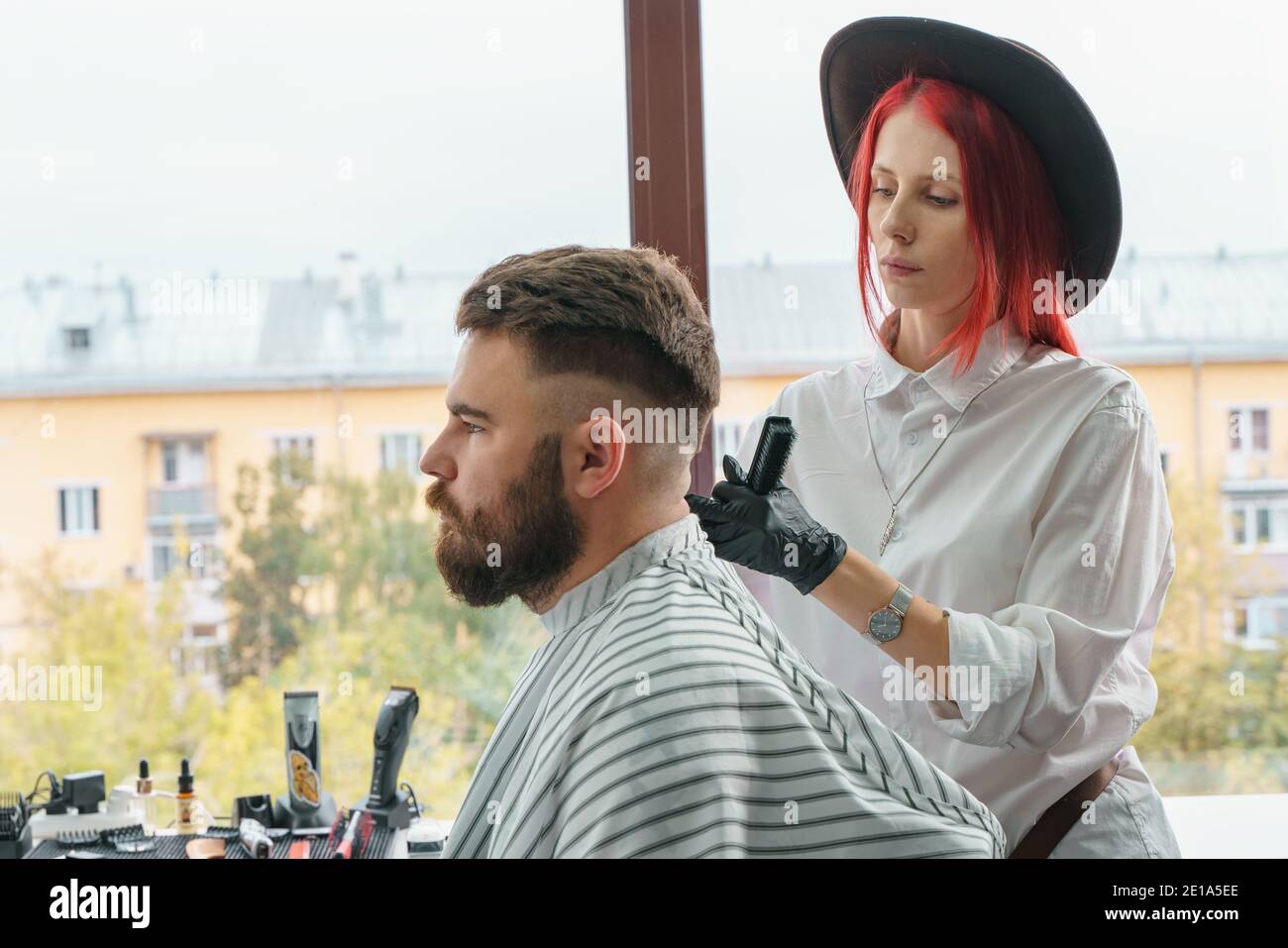 Professional hairdresser uses a hair clipper for fringing beard for a handsome man in barbershop Stock Photo