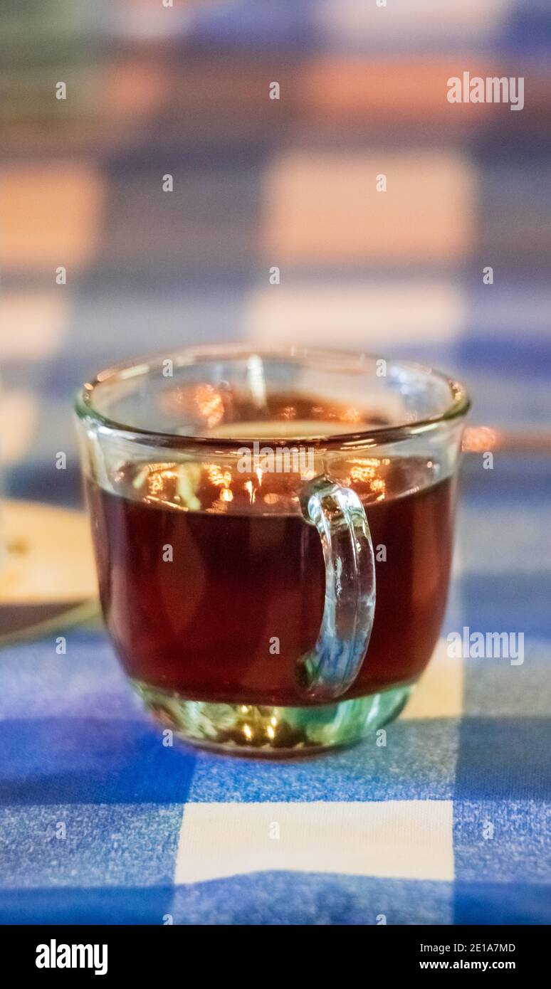 A hot delicious cup of tea on a transparent cup over a table with a blue and white tablecloth Stock Photo