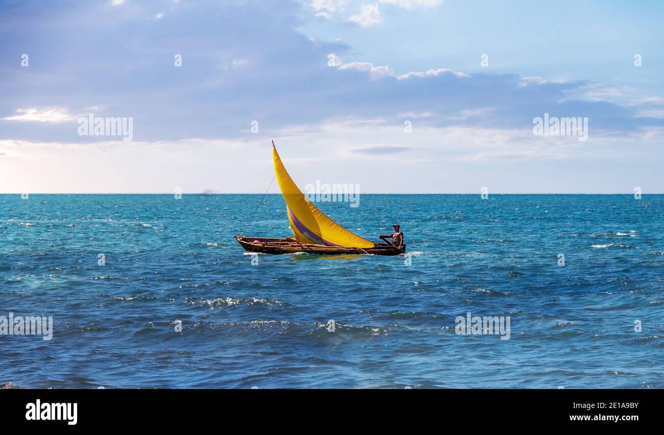 A Sailingboat sailing alone in the middle of huge a peaceful ocean, rising its colorful sails to allow the wind give its gently energy. Stock Photo