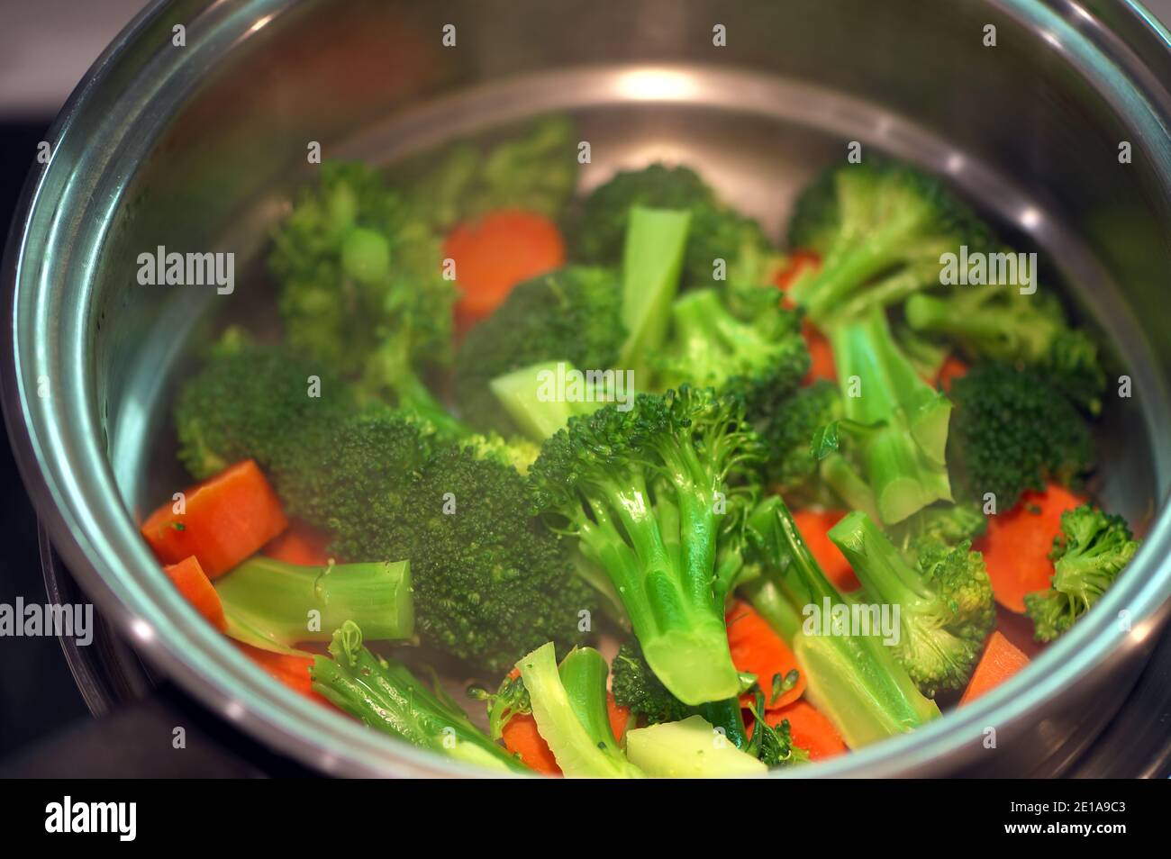 Steamed broccoli and carrots in a stainless steel double boiler on the stove top. Stock Photo