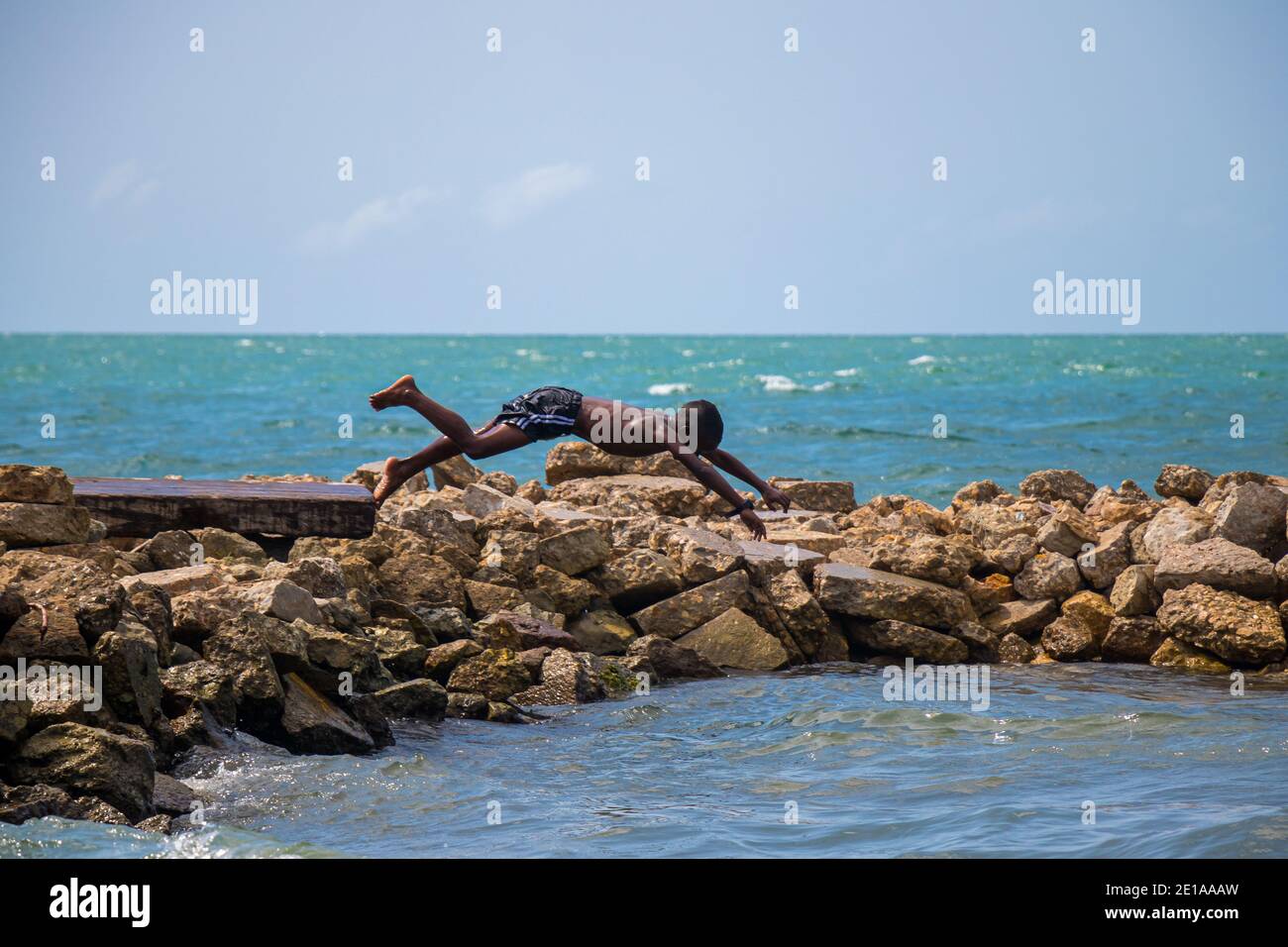 Boy is enjoying the fresh water on a peaceful beach jumping from the rocks to the water Stock Photo