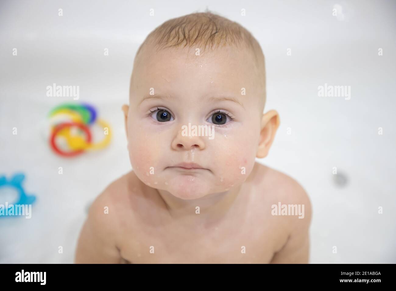 Cute baby girl bathing with toys and smiling in a big white bath Stock