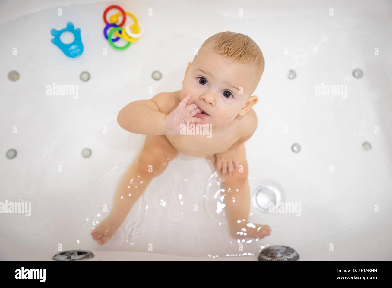Cute baby girl bathing with toys and smiling in big white bath Stock