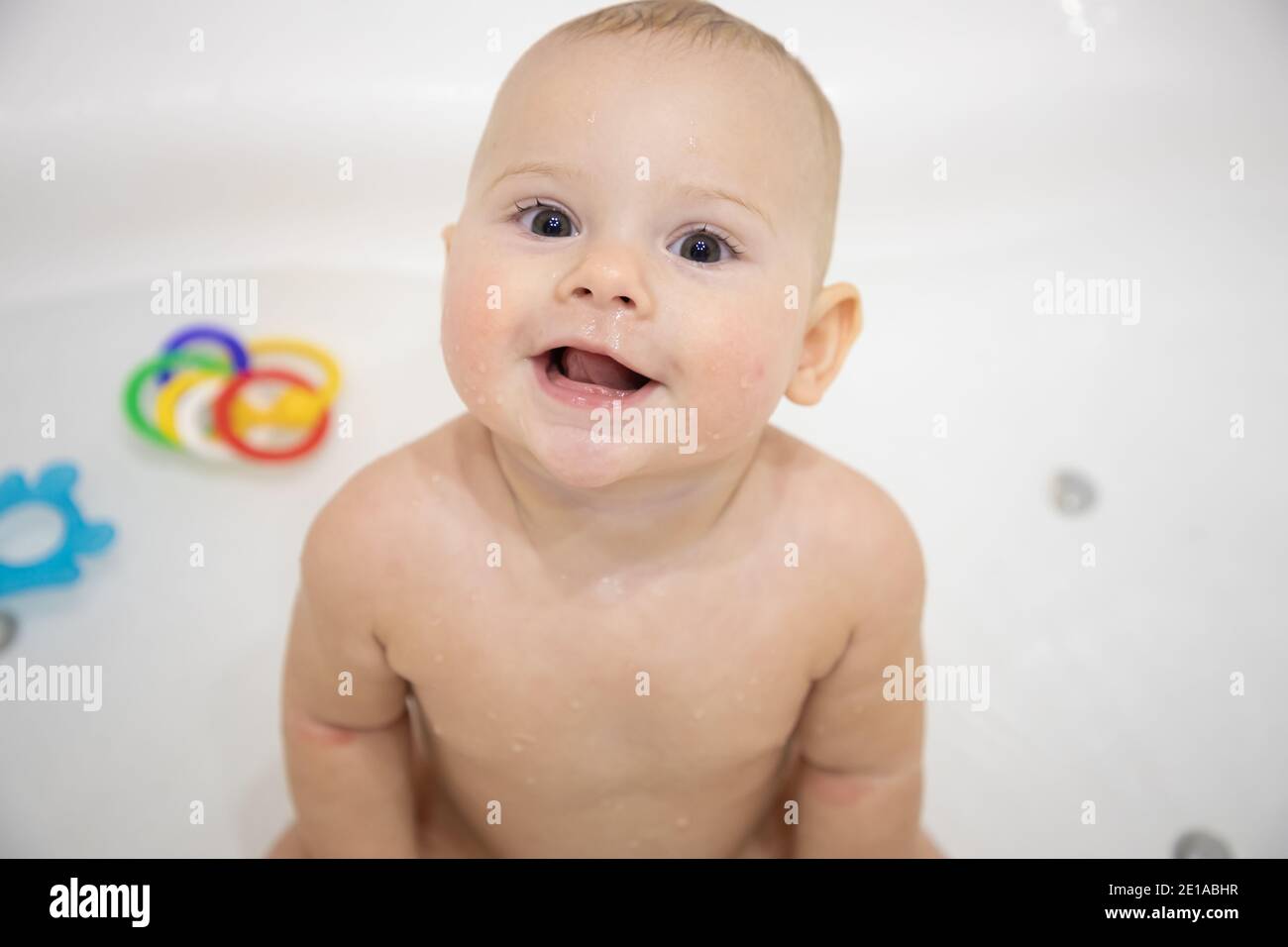 Cute baby girl bathing with toys and smiling in big white bath Stock