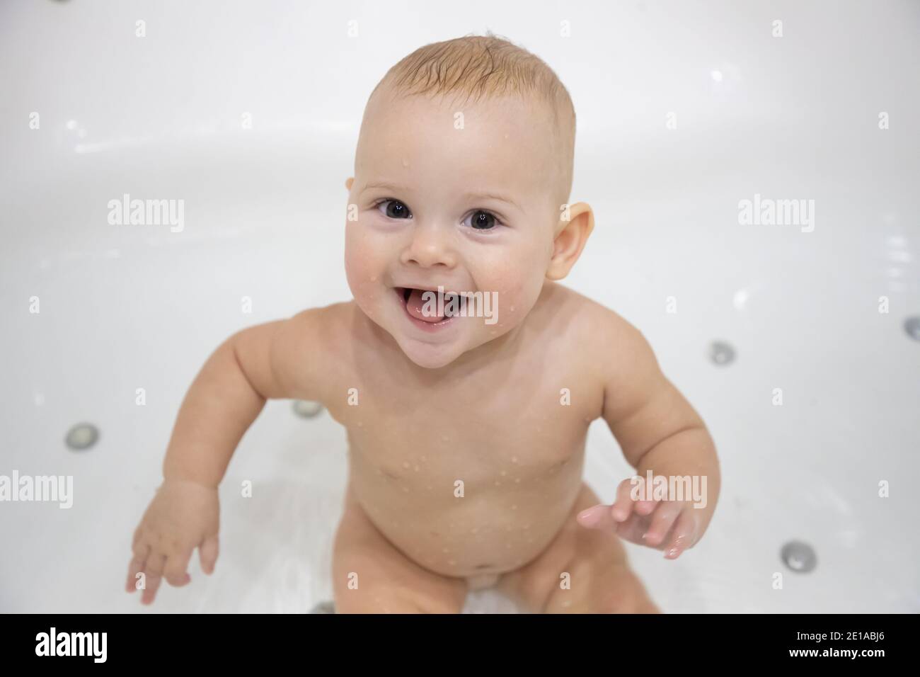 Cute baby girl bathing with toys and smiling in big white bath Stock