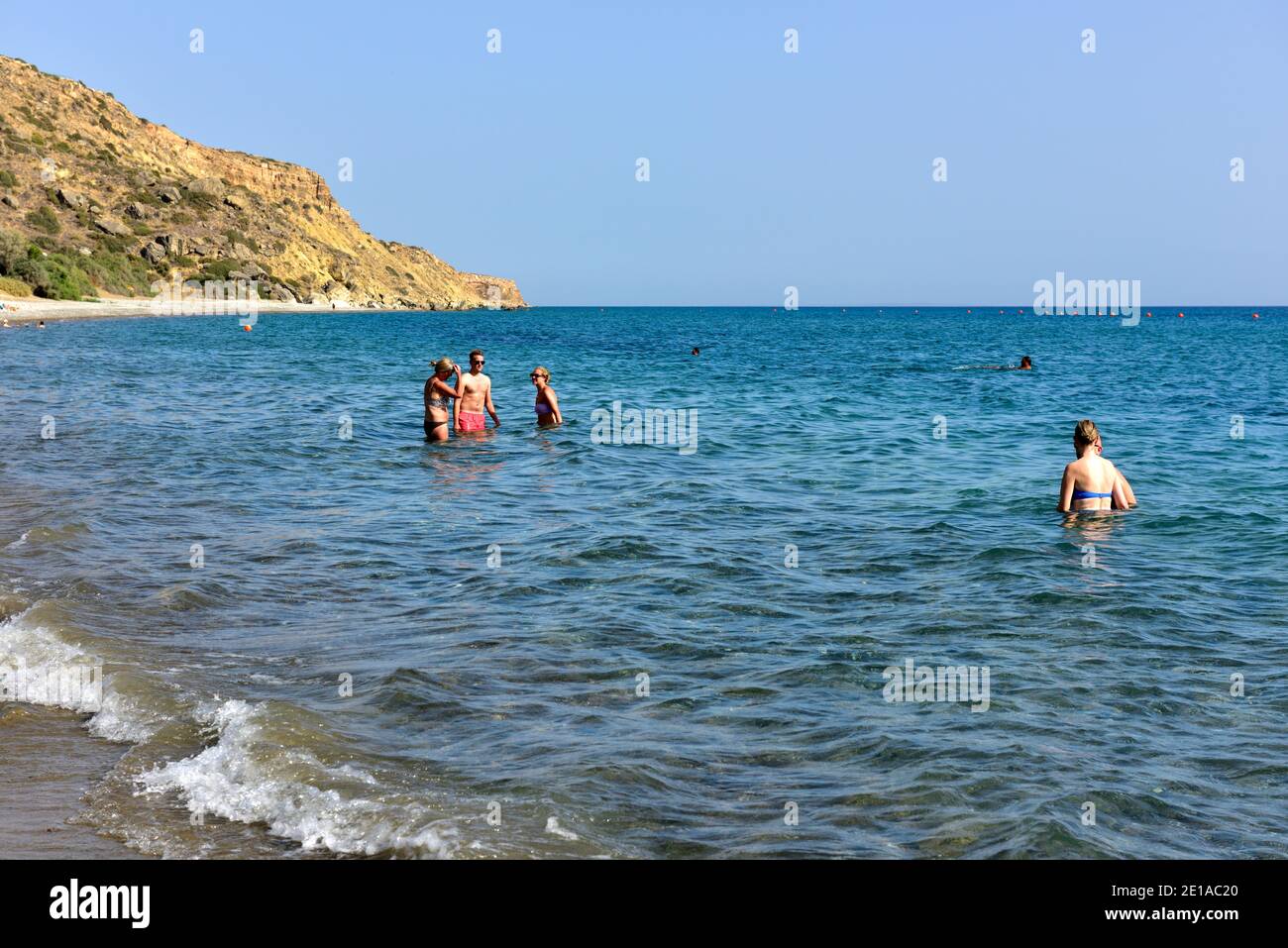People standing in the calm blue sea off beach others swimming further out Stock Photo