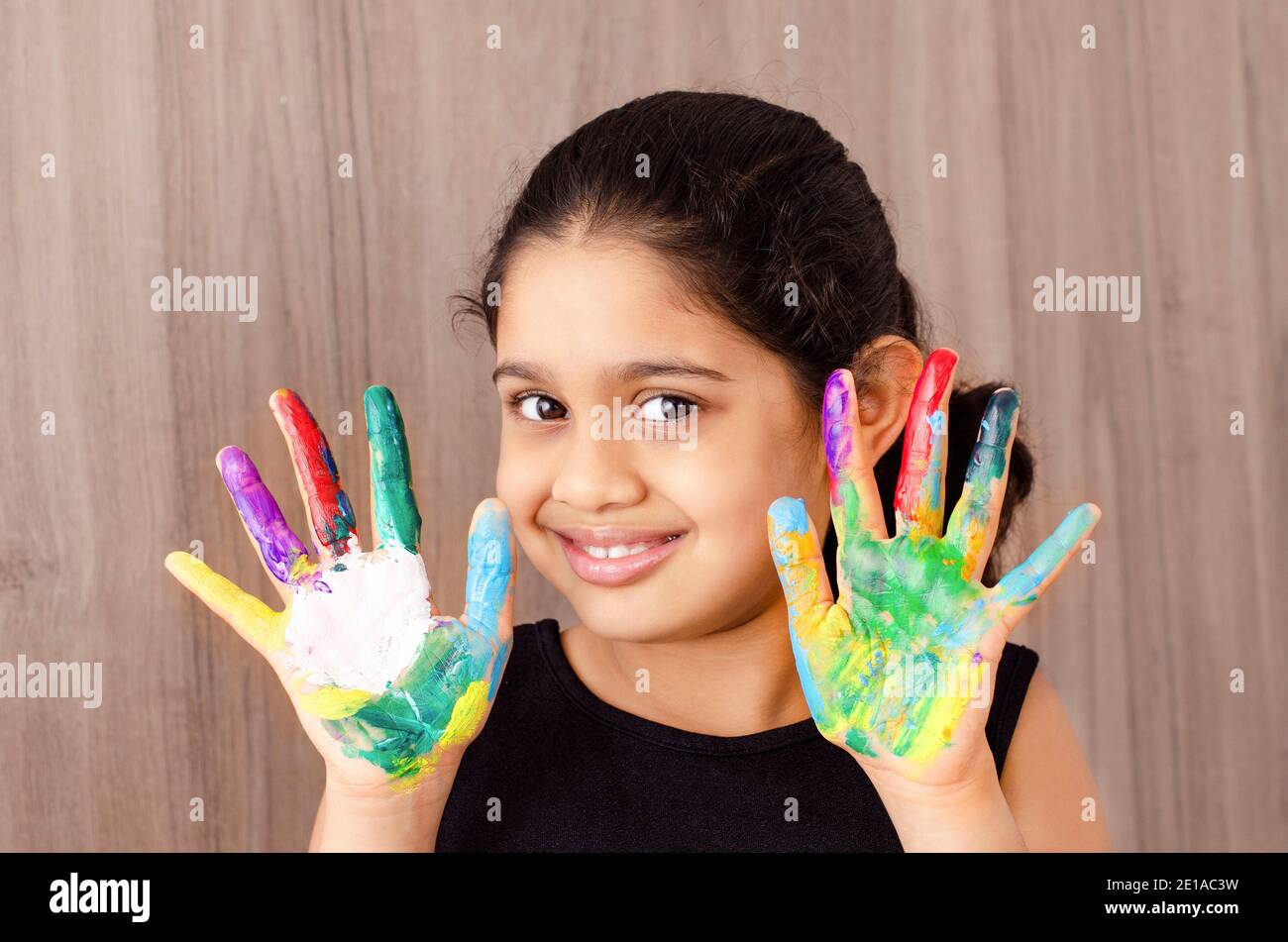 Portrait of a happy and smiling Indian kid having fun by playing with different colored paints in her finger. Stock Photo
