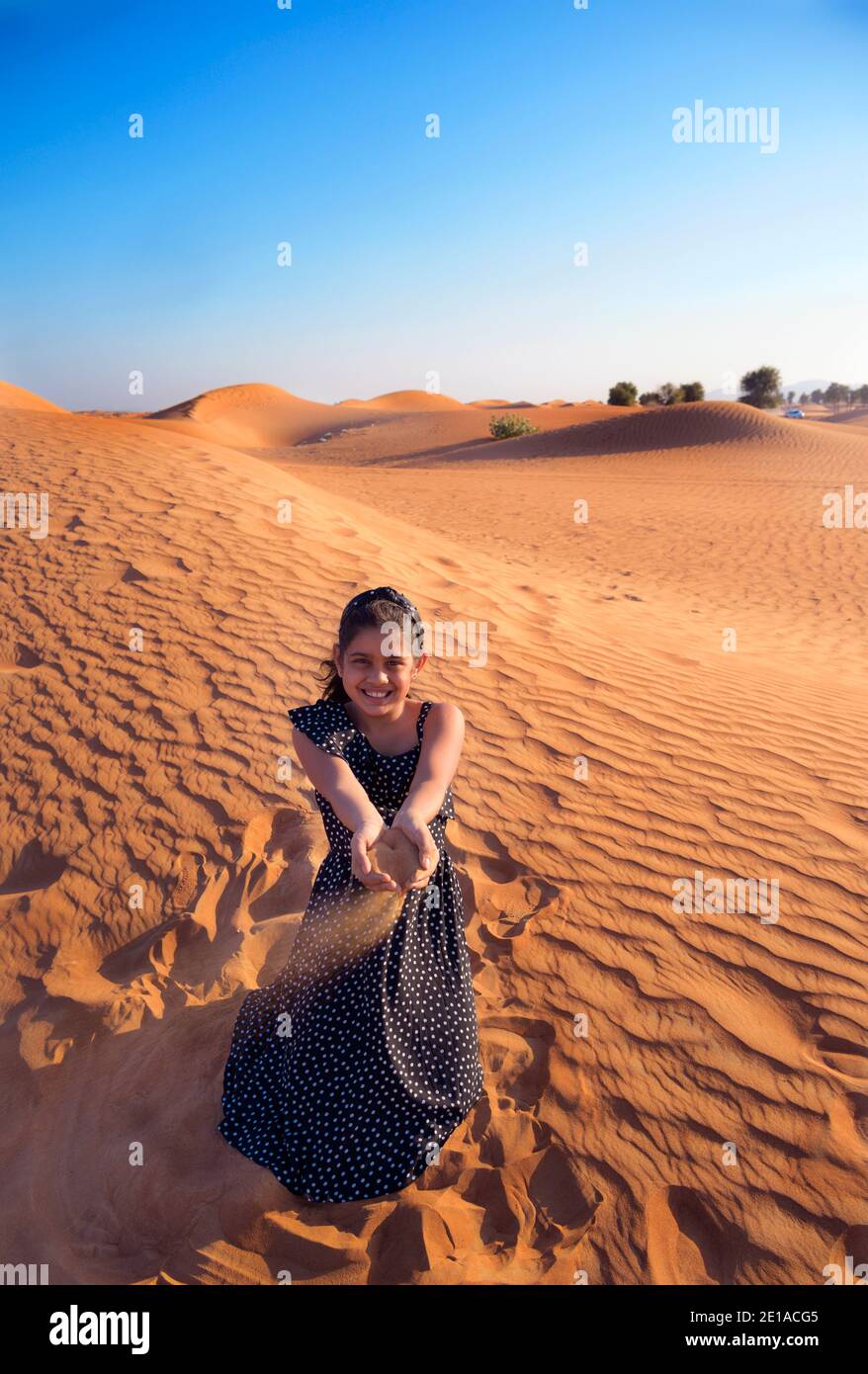 A happy little Indian girl playing in dunes in desert by blowing the sands and enjoying the vacation in Dubai ,United Arab Emirates Stock Photo