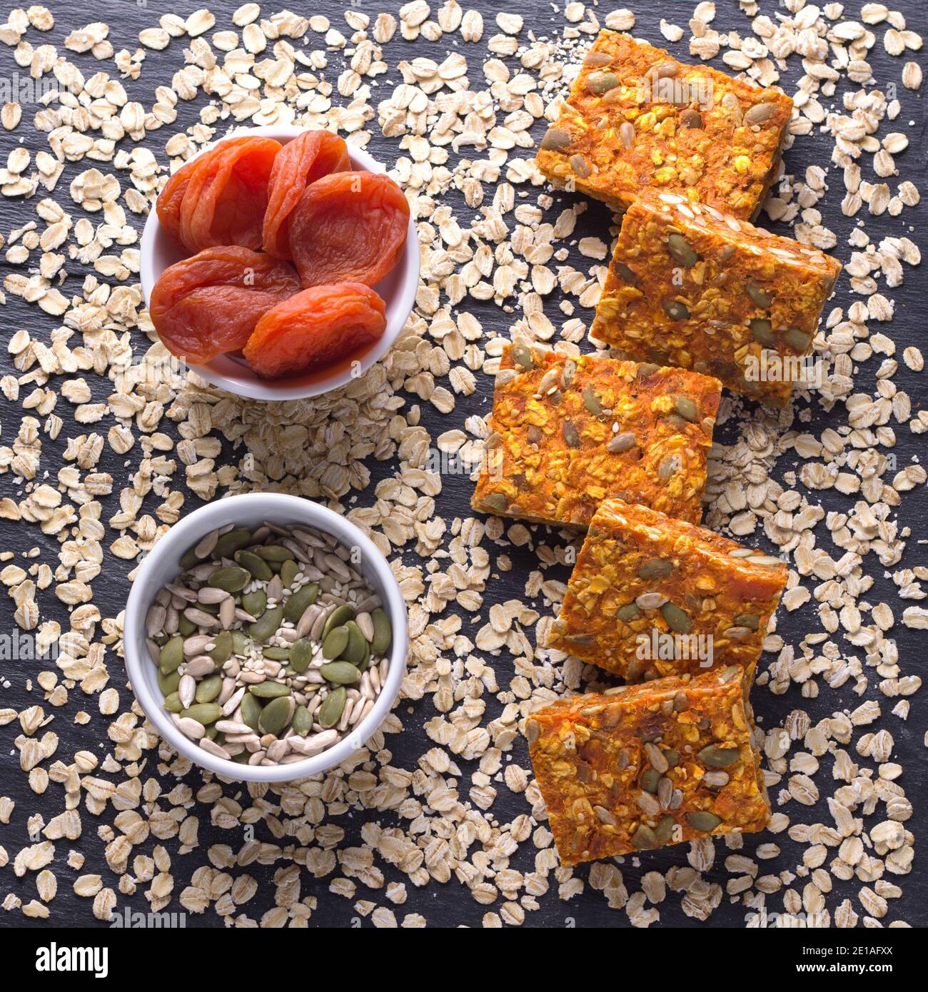Carrot bars with oatmeal, dried apricots, seeds and honey on a gray shale background, selective focus, top view. Healthy energy snack Stock Photo