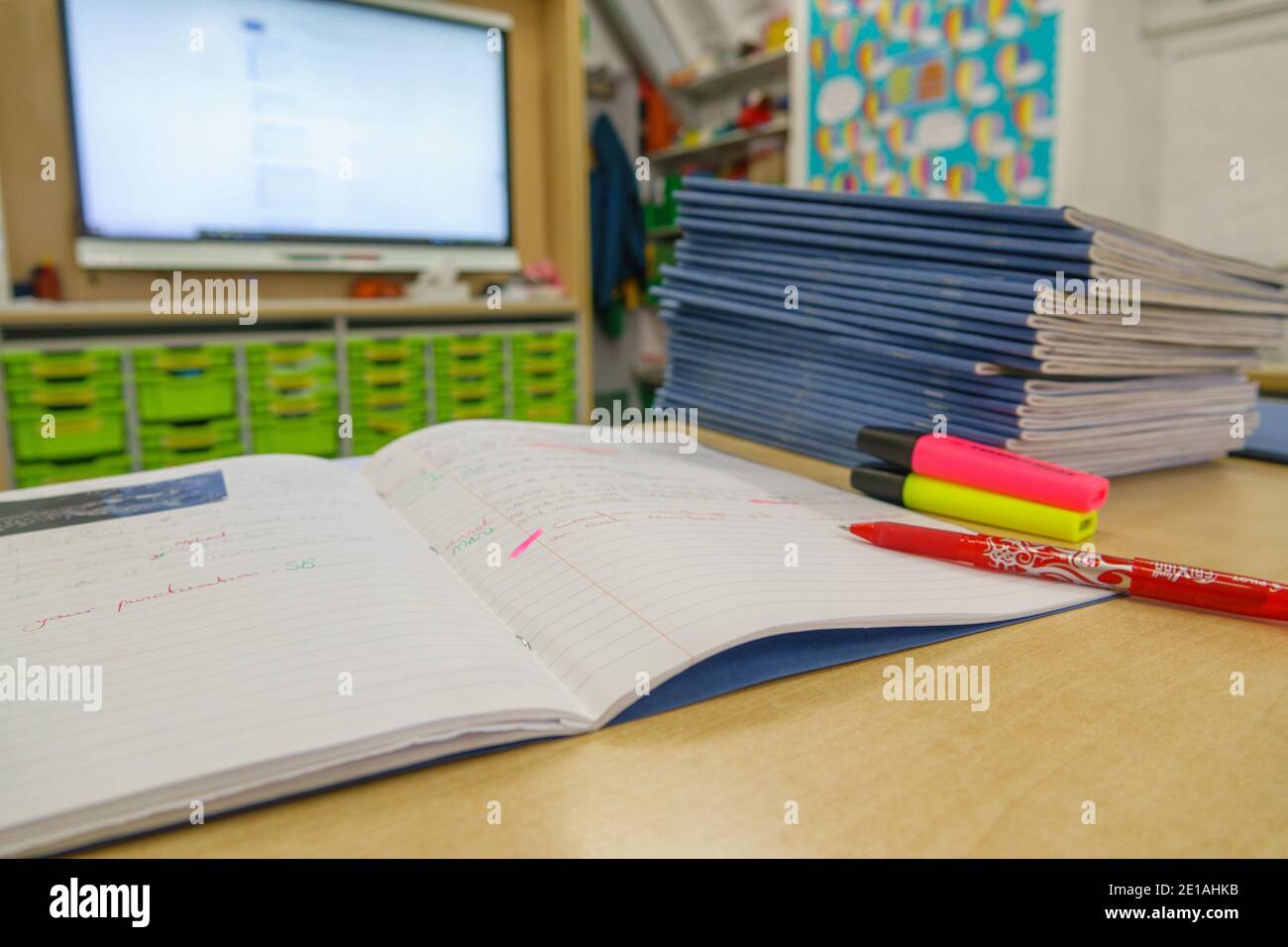 Pile of school books, on a desk, that a teacher is marking, in an empty primary classroom, with red pen. London, UK. Stock Photo