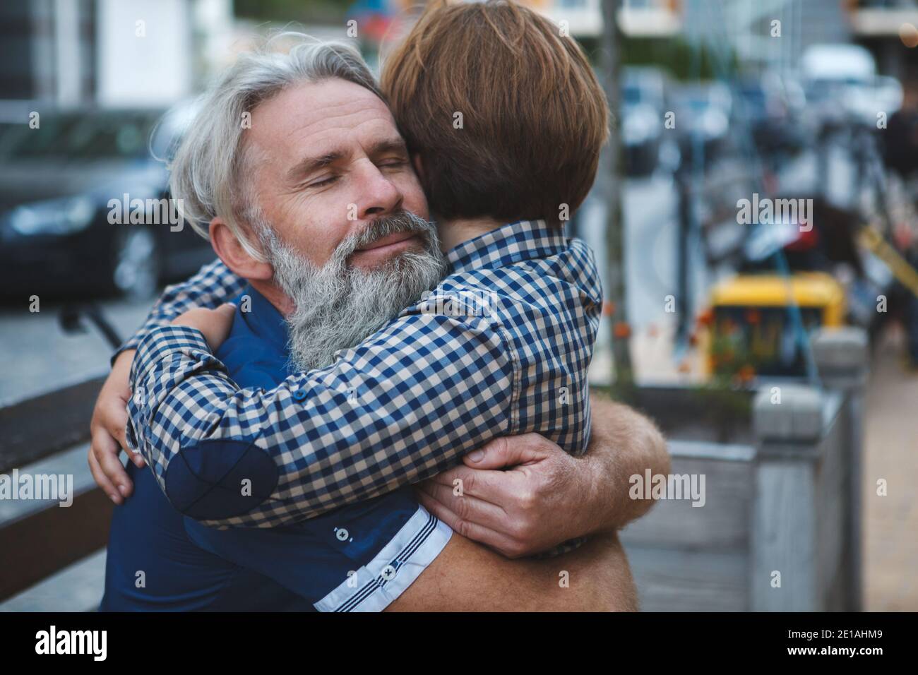 Close up of a happy elderly bearded man smiling with his eyes closed, embracing his young grandson Stock Photo