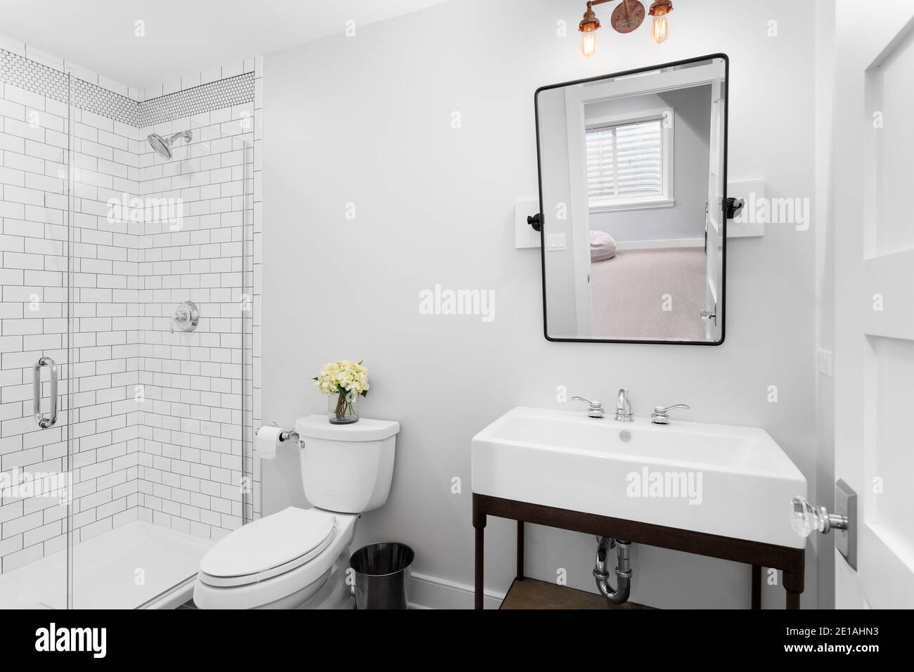 A luxurious modern farmhouse bathroom with a tilting mirror, pedestal sink, and a subway tiled white shower. Stock Photo