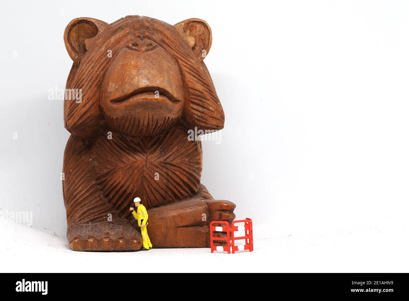 See No Evil wooden monkey ornament being cleaned up by tiny workmen. Stock Photo
