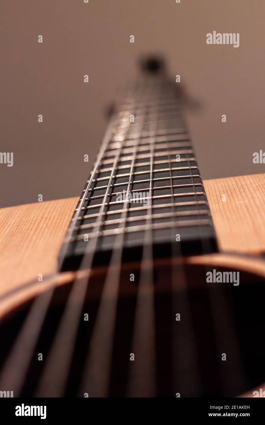 Closeup shot of a guitar neck, taken from behind, with blurry front end of guitar, and a blurred wall, creating an aura of melancholic beauty Stock Photo