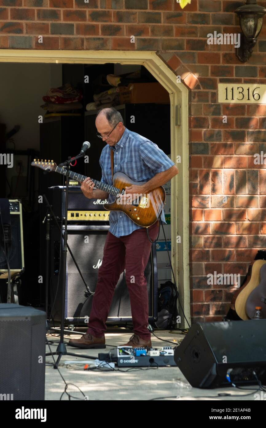 Adult man in a garage band practicing for a gig or engagement on a driveway in front of a garage during the summer. USA Stock Photo