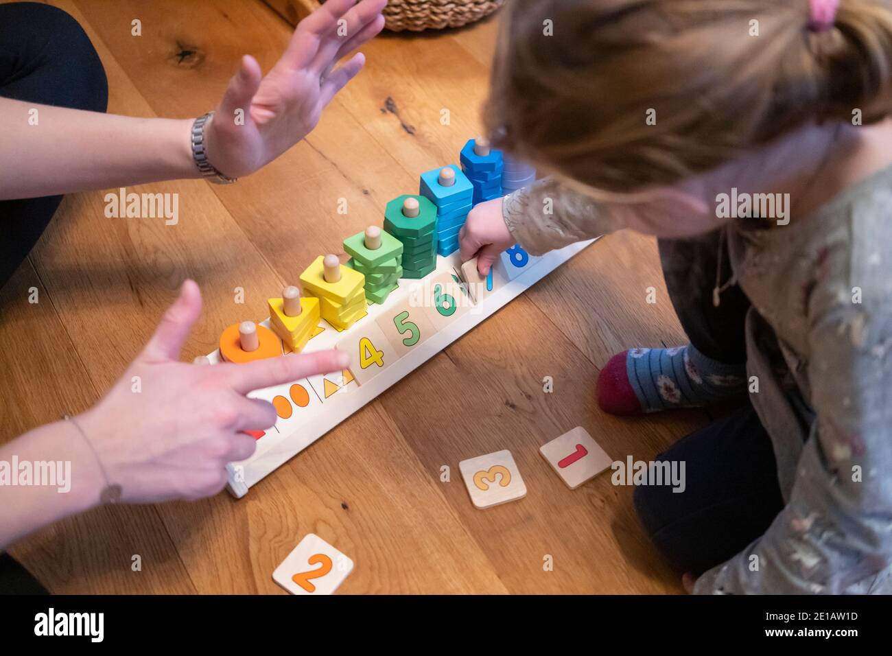 A mother holding up her fingers to show her two year old daughter which number to place, using a counting shapes stacker educational toy Stock Photo