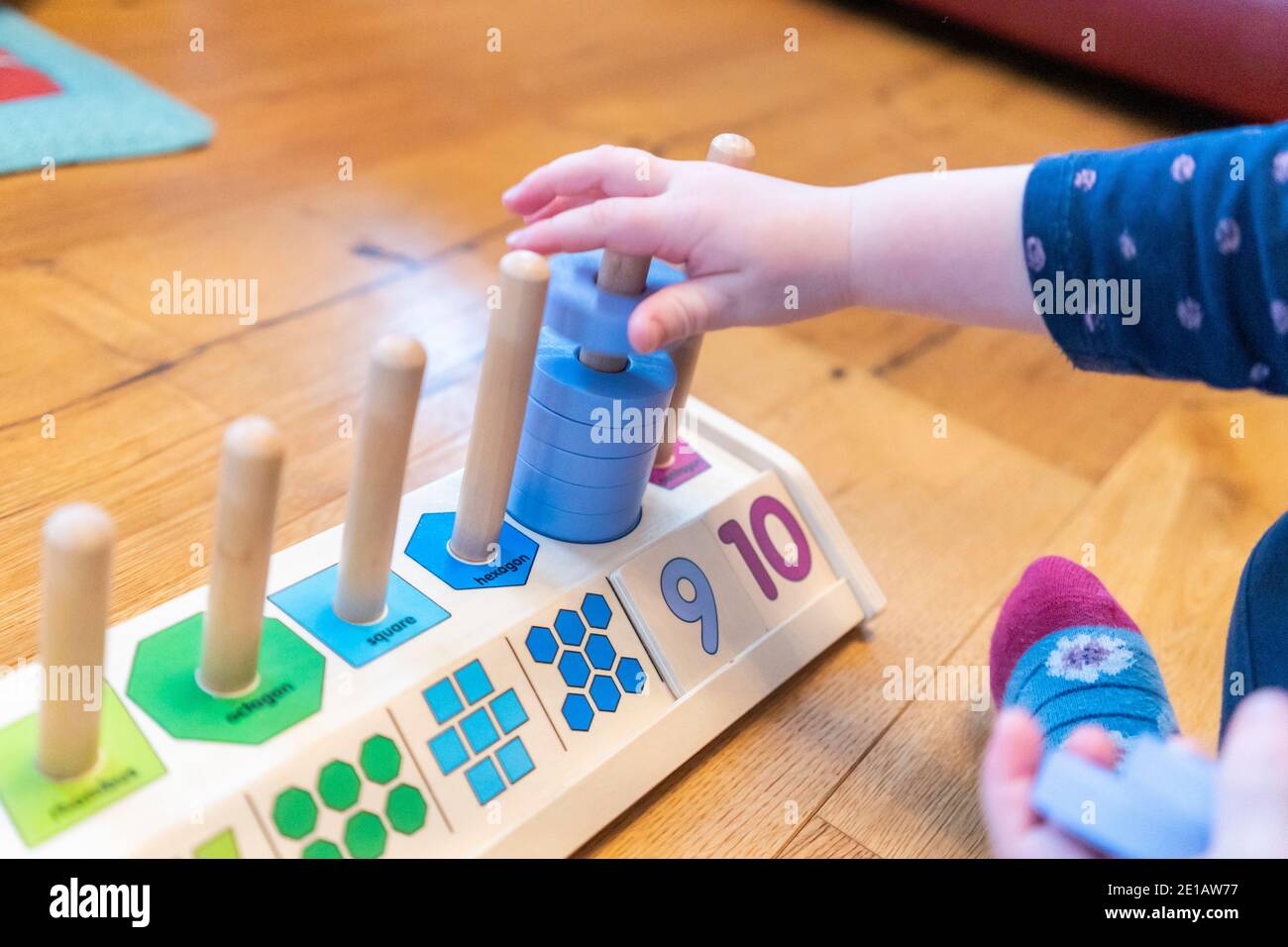 A young two year old child sitting on the floor and learning to count with a wooden counting shapes stacker educational toy Stock Photo