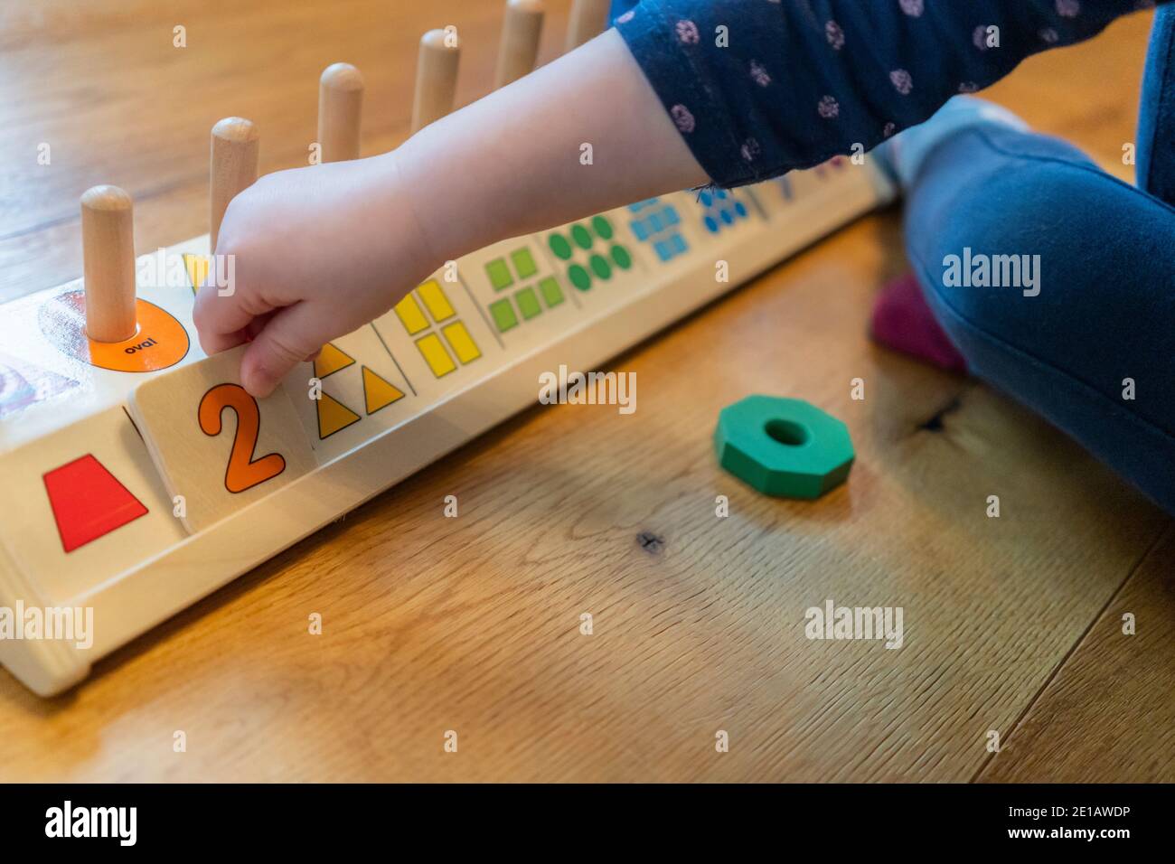 A young two year old child sitting on the floor and learning to count with a wooden counting shapes stacker educational toy Stock Photo