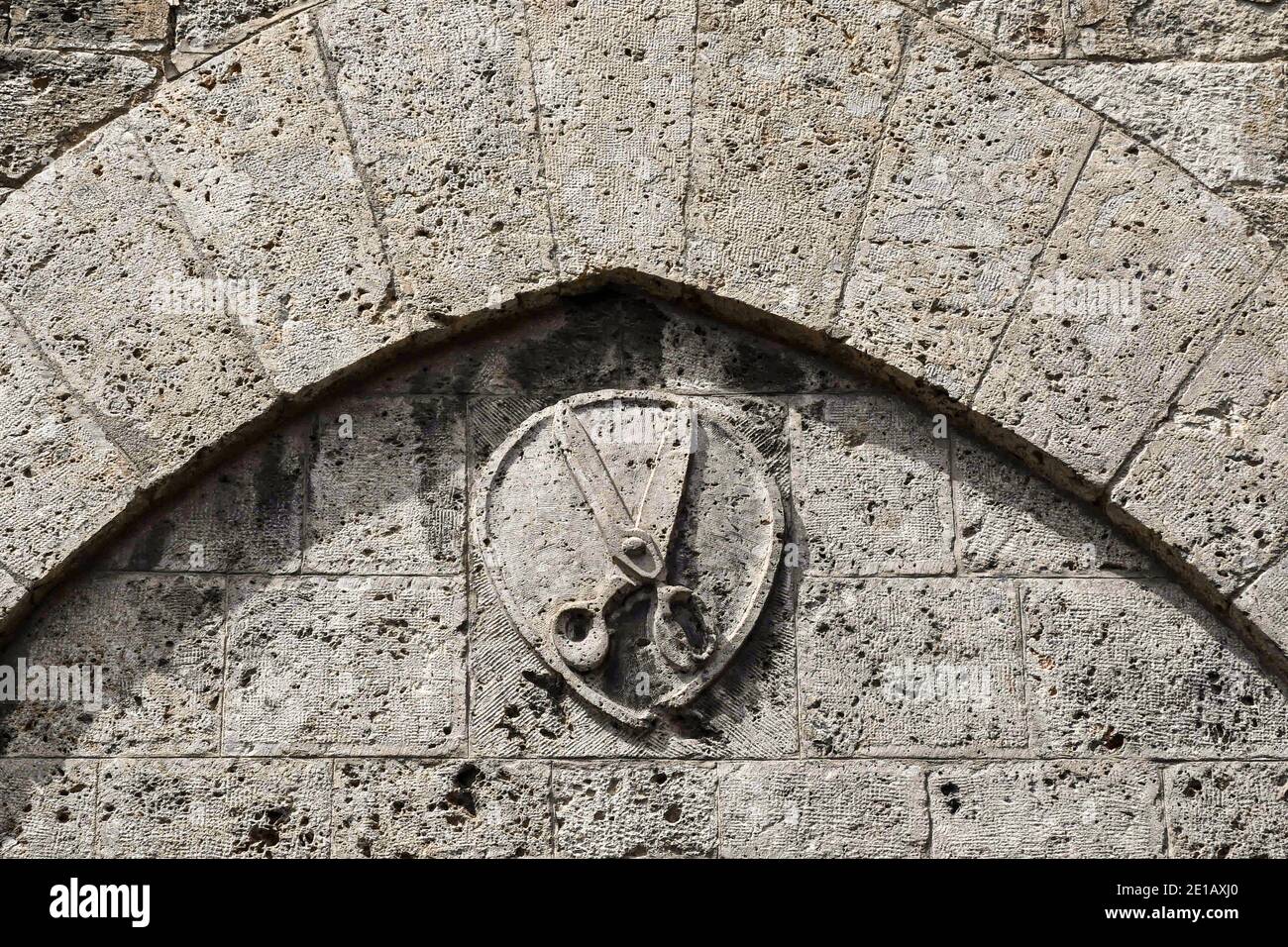 Close-up of an ancient stone bas-relief depicting a scissors, symbol of the barbers, in the old town of Siena, Tuscany, Italy Stock Photo
