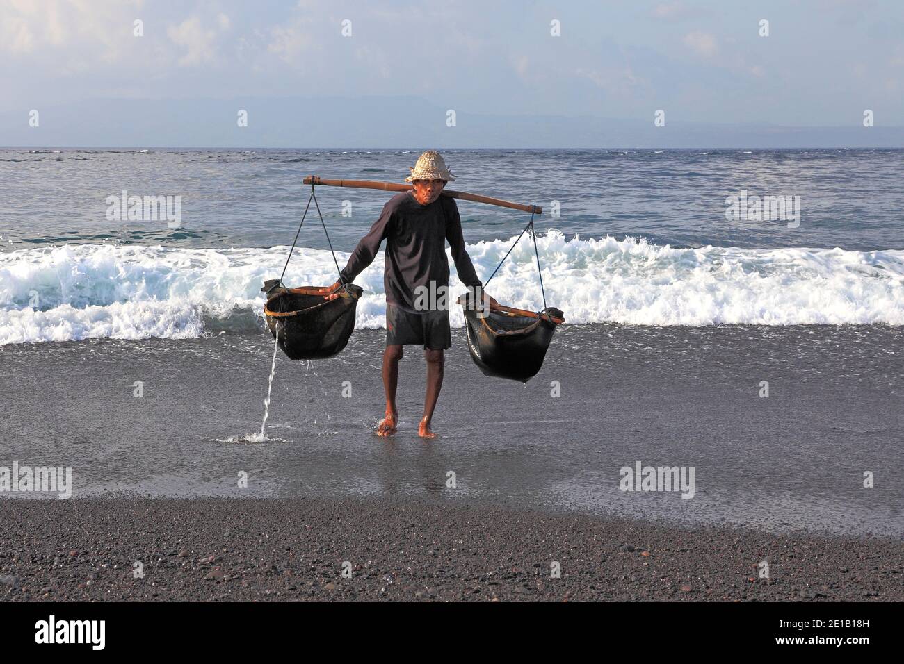 One of the few remaining traditional salt makers in Bali, at Kusamba Beach. Bali, Indonesia. Workers start before sunrise to water the sand with sea w Stock Photo