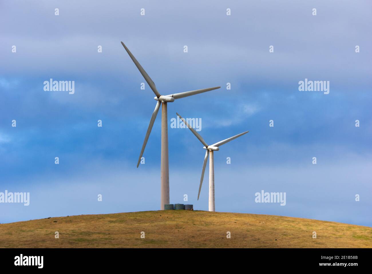 Wind turbines and rotors sit on a hill among a blue sky generating ...