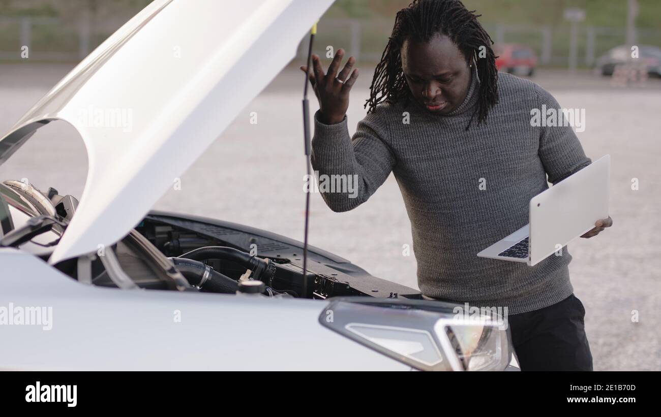 Young african american black man repairing the car while using laptop as diagnostic tool. High quality photo Stock Photo