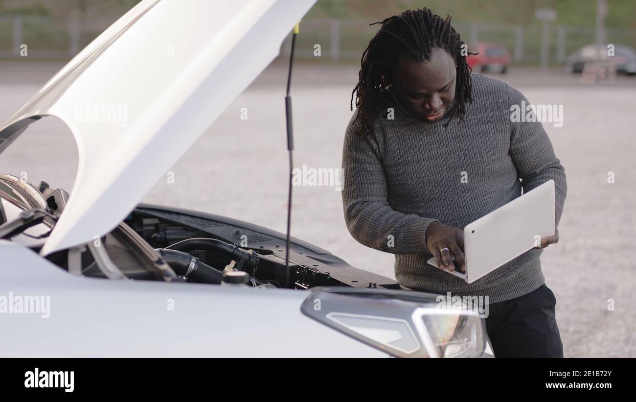 Mobile car assistance. African american black man running diagnostic on broken car on his laptop. High quality photo Stock Photo