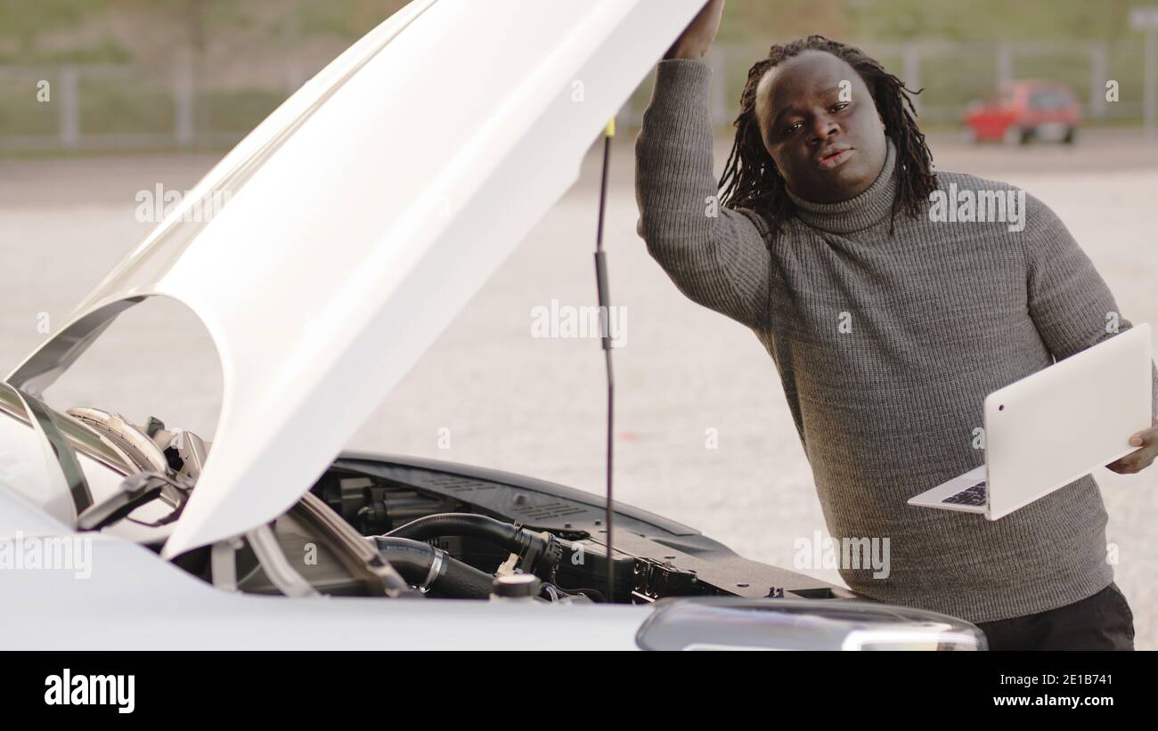 Mobile car assistance. African american black man running diagnostic on broken car on his laptop. High quality photo Stock Photo