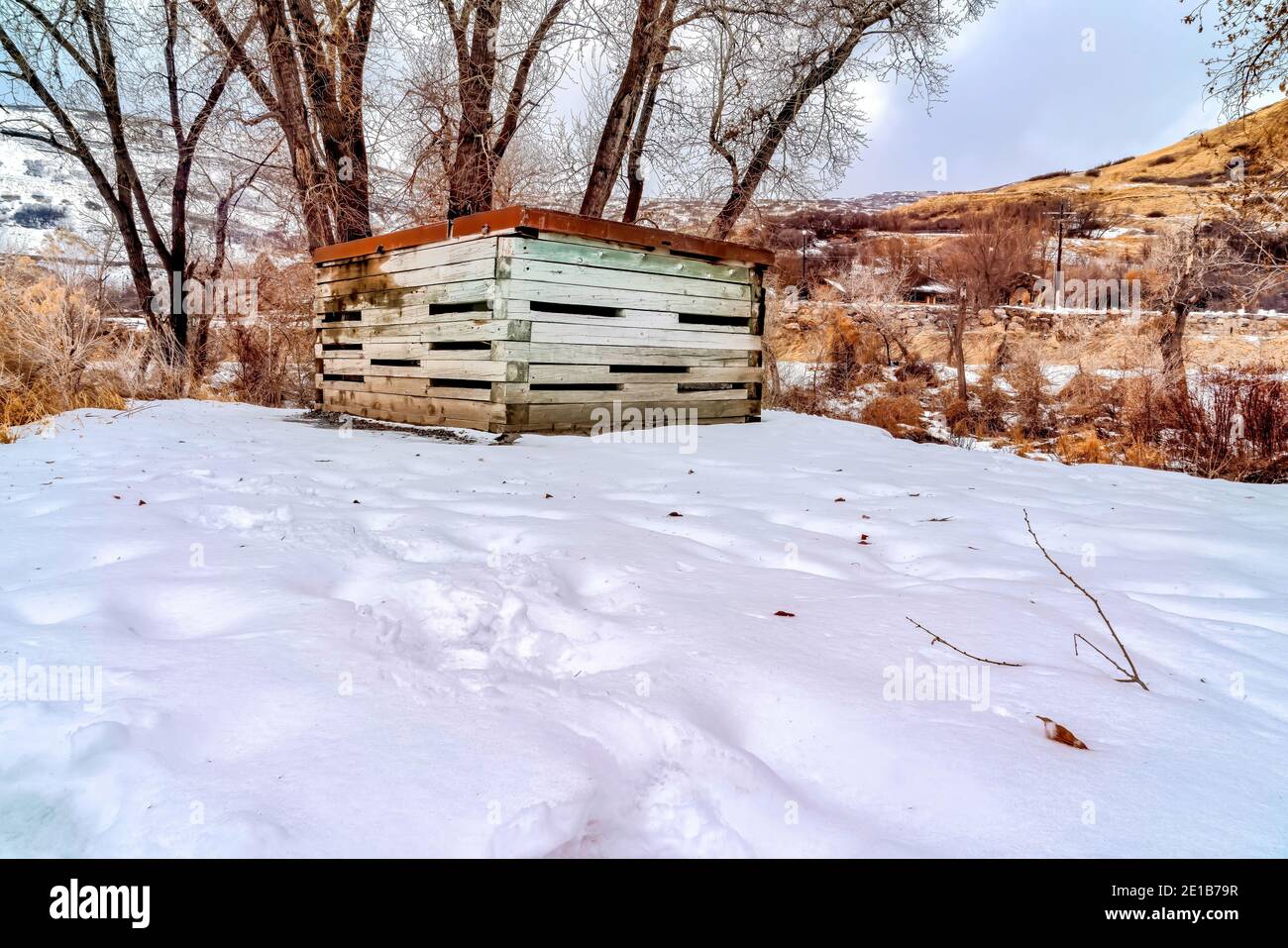 Wooden storage shed with rusty metal roof on snow covered landscape in