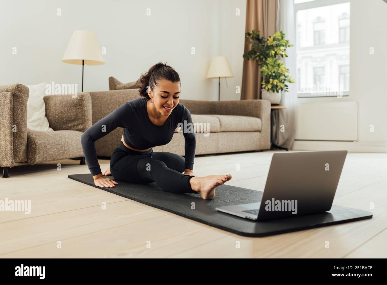 Female doing stretching workout while watching online videos on laptop indoors Stock Photo