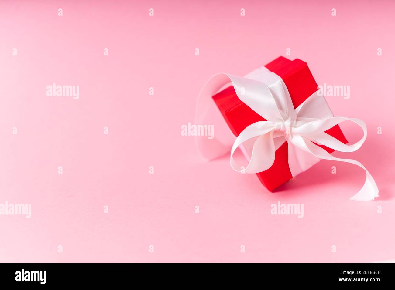 small red gift box with white ribbon and bow on pink background ...
