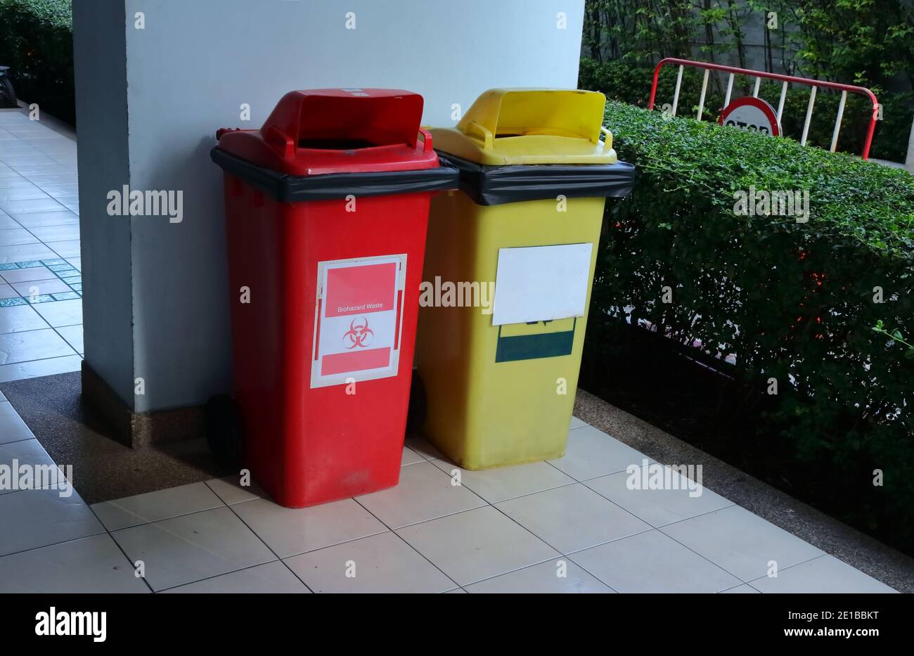 Closeup biohazard bin next to yellow recycling bin against blue wall Stock Photo