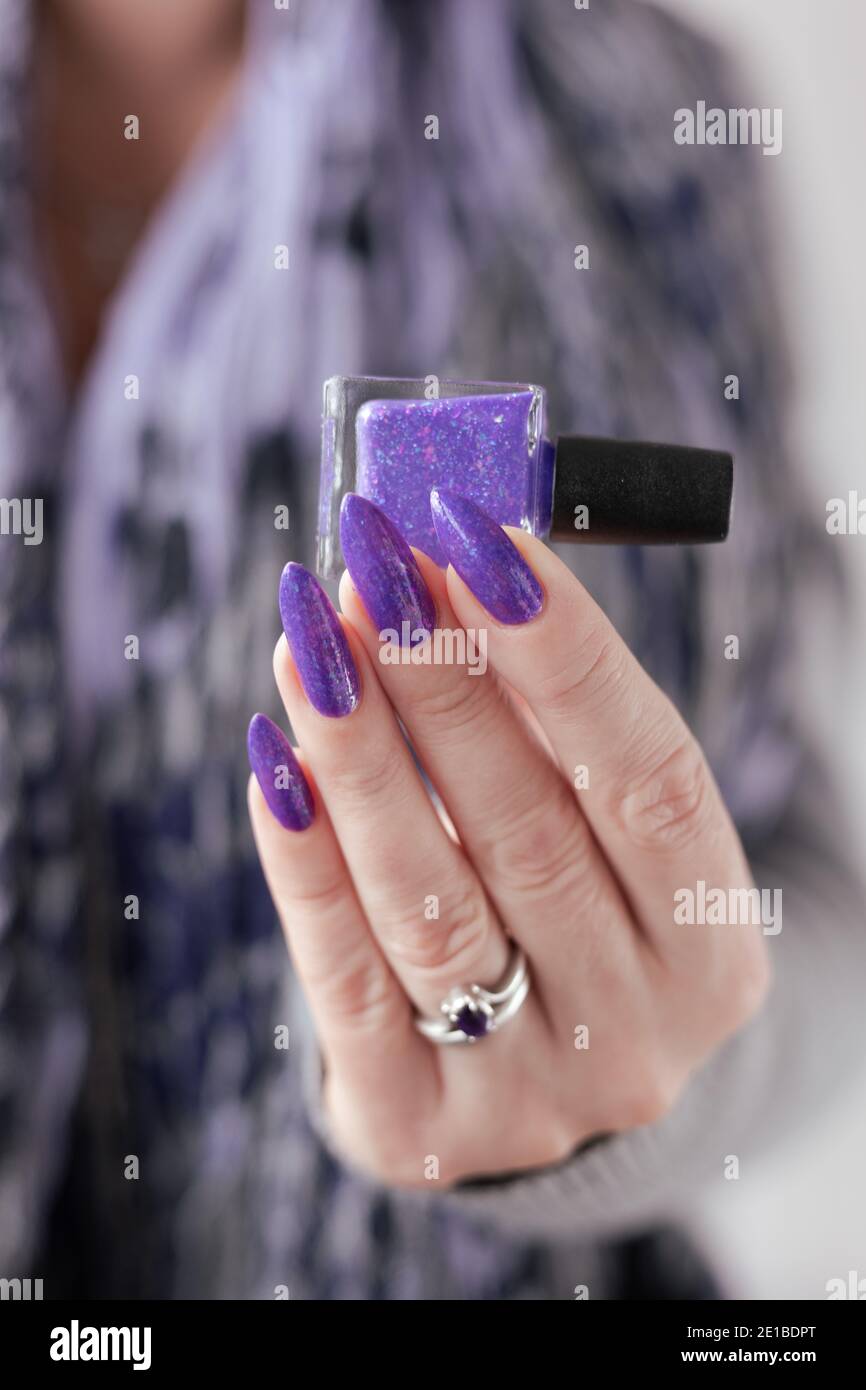 Female hand with long nails and purple lilac manicure holds a bottle of nail  polish Stock Photo - Alamy