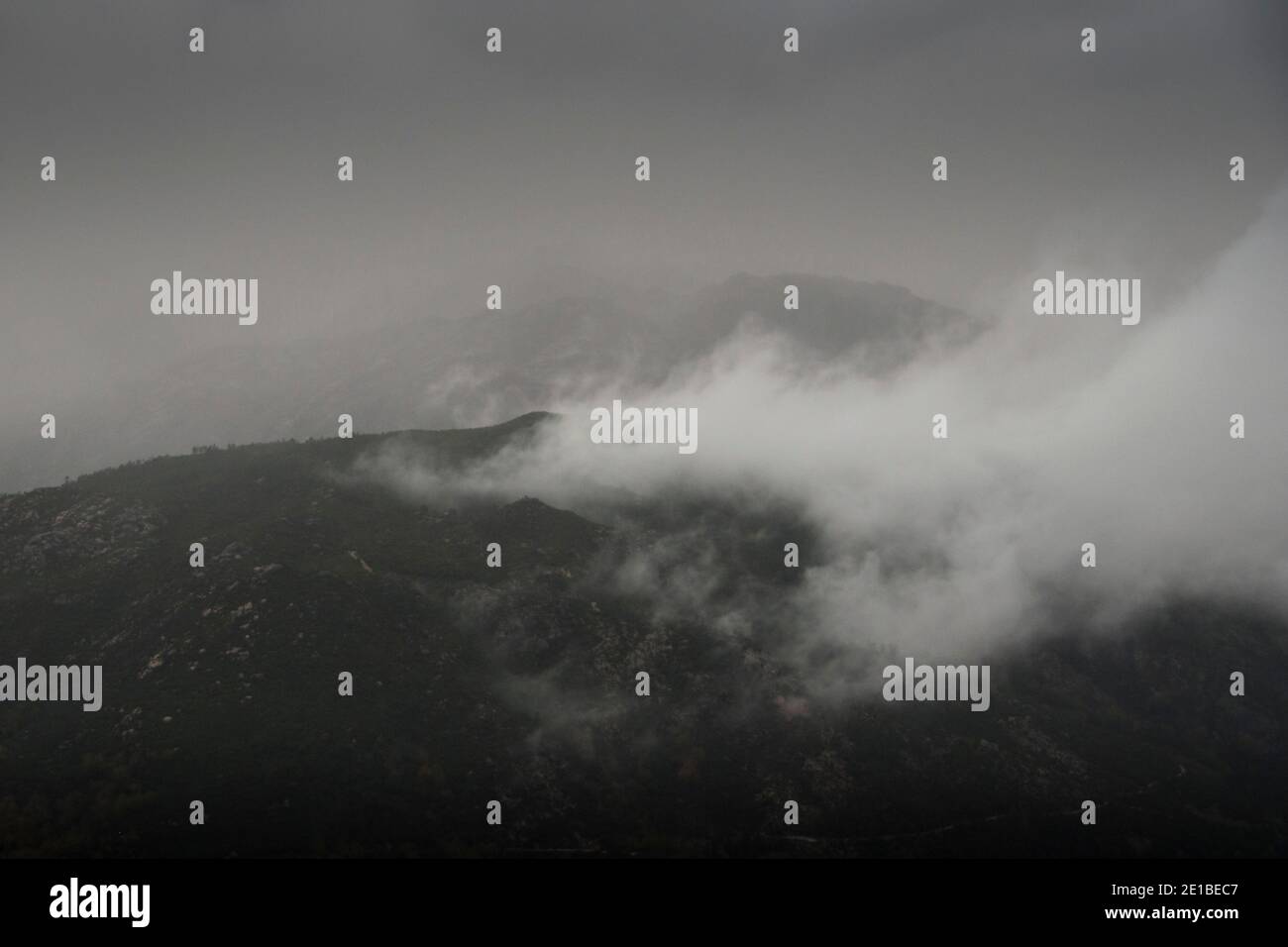 Low clouds lifting up from the mountains in a dark rainy day Stock Photo