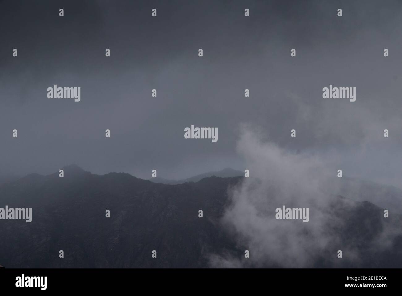 Low clouds lifting up from the mountains in a dark rainy day Stock Photo