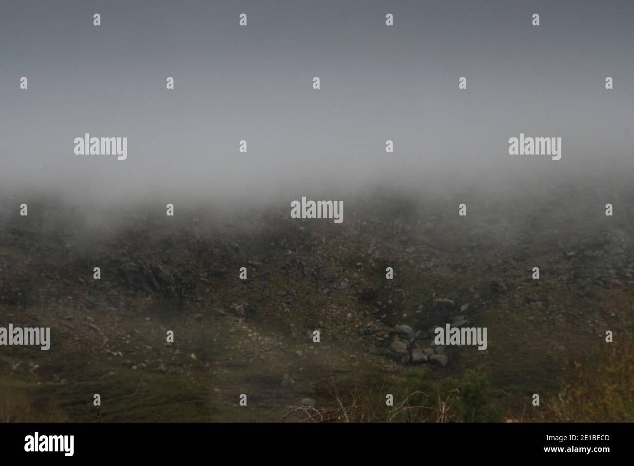 Low clouds and fog lifting up from the mountains in a dark rainy day Stock Photo