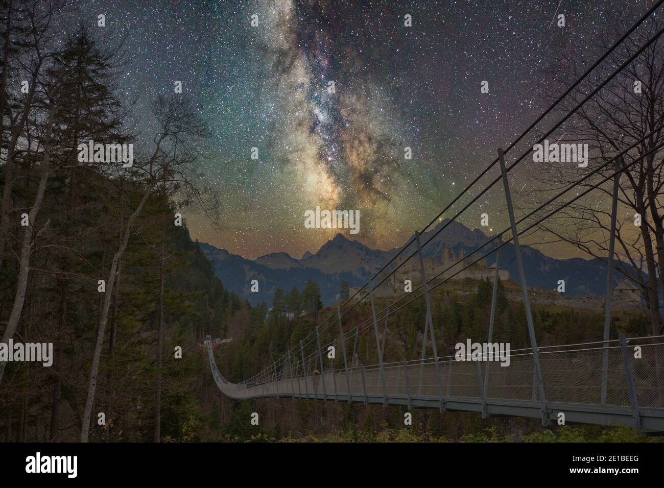 Suspension bridge with trees in front of mountains and a castle with milky way Stock Photo