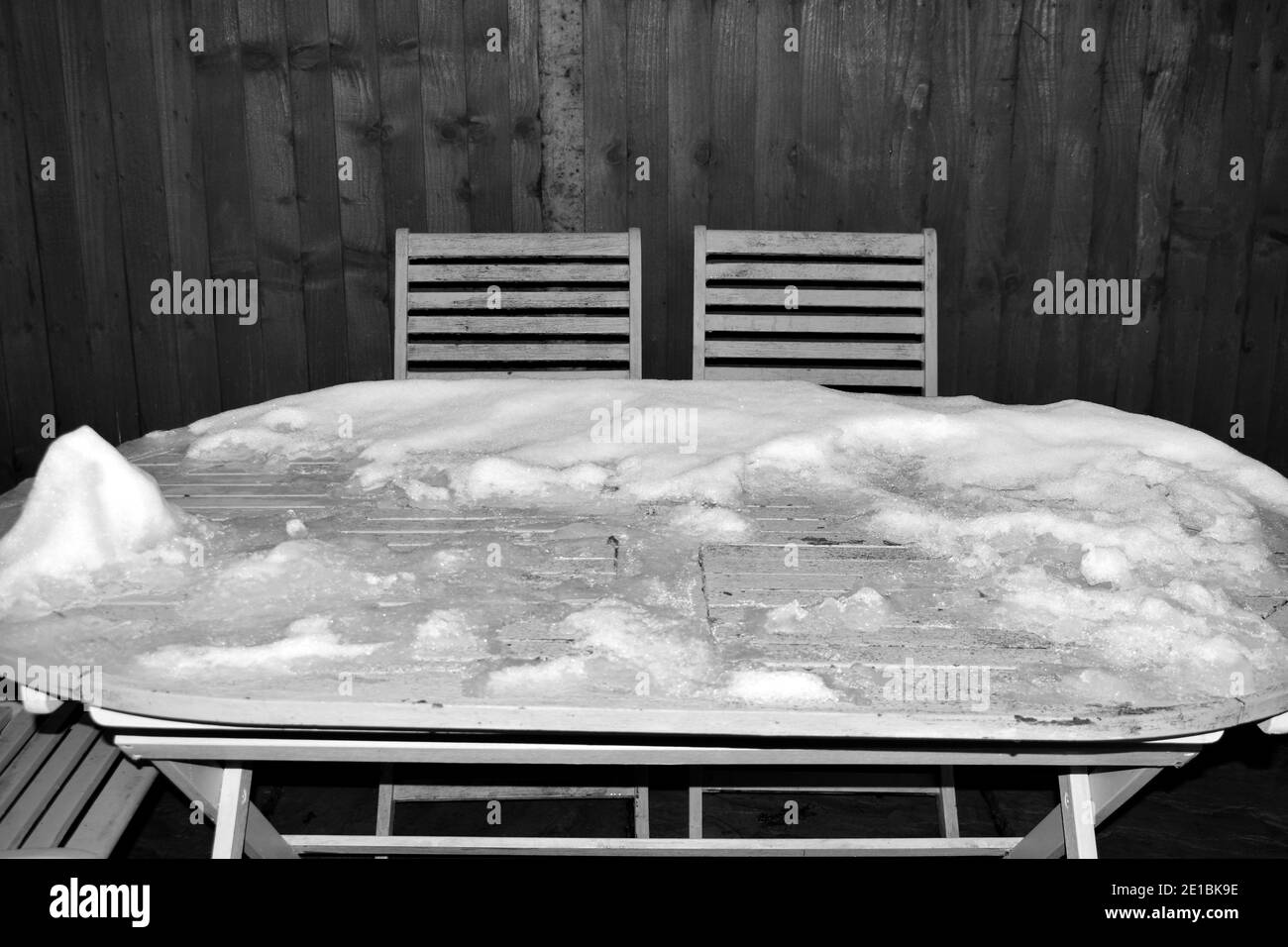 close up of black and white image of snow covered rustic woodentable with empty chairs outside in  winter time Stock Photo