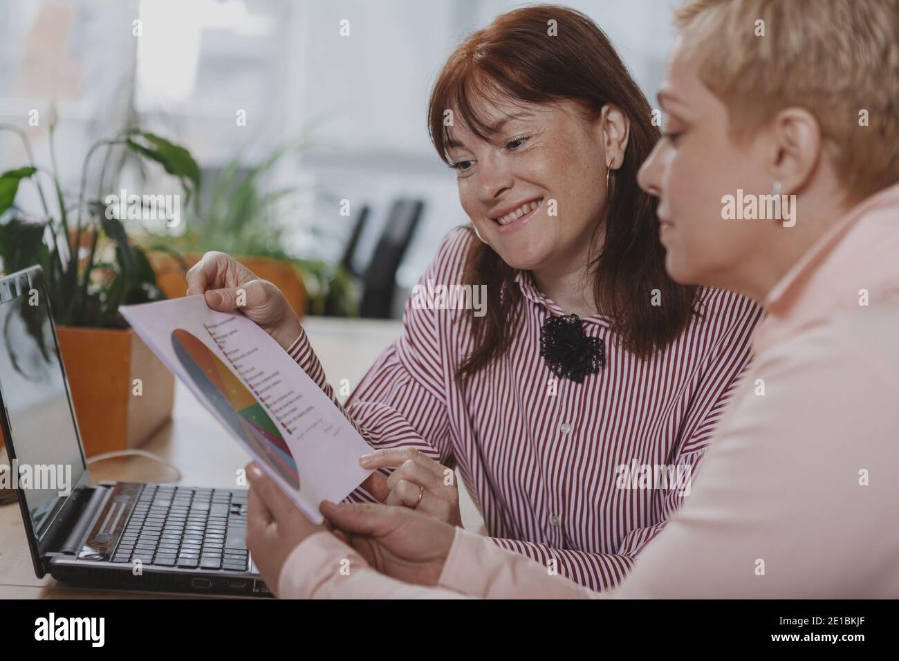 Two mature businesswomen concentrating over paperwork at the office. Female entrepreneurs discussing statistics at work, examining documents, copy spa Stock Photo