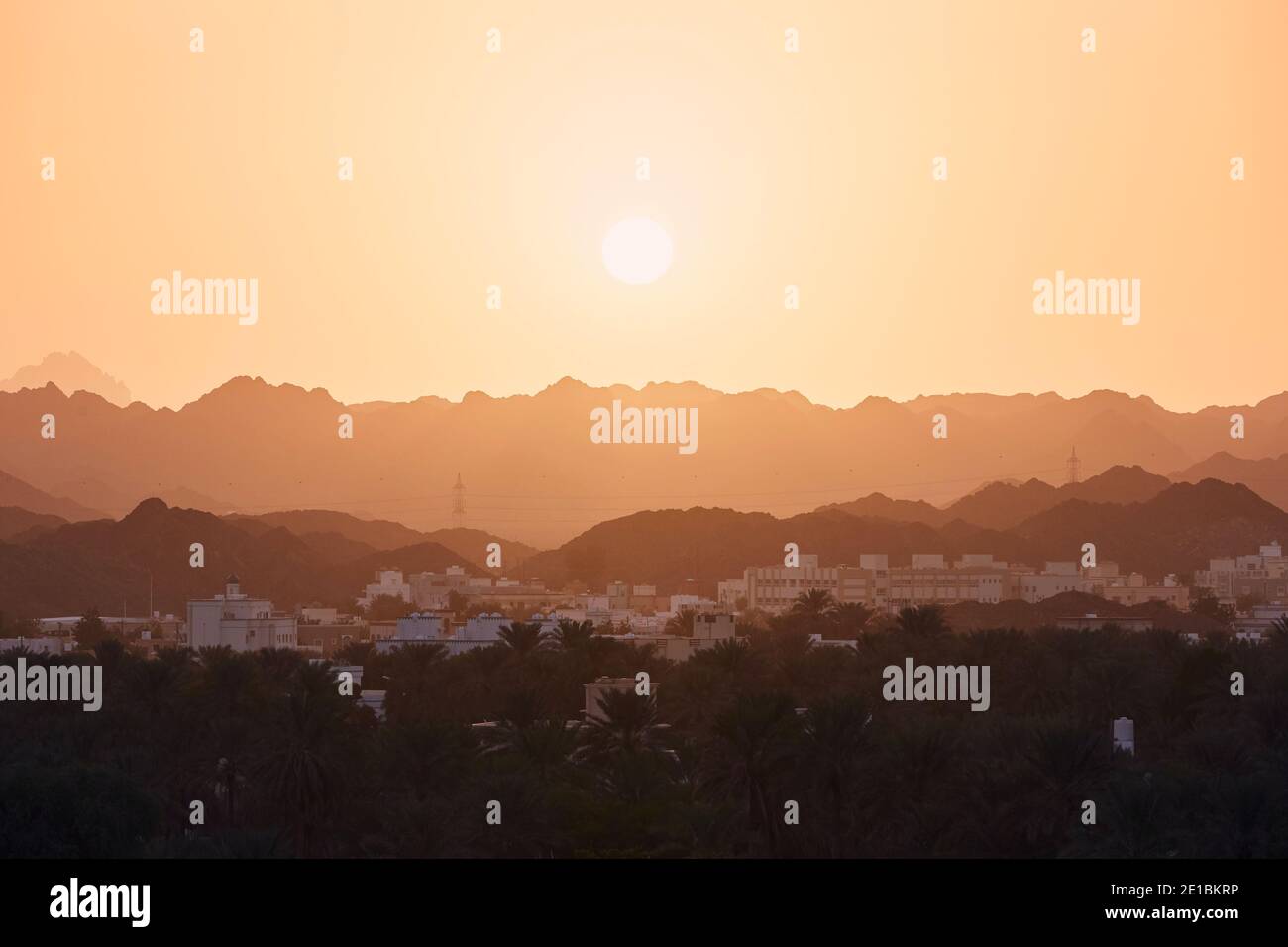 Sun above old city against mountain range. Nizwa in Sultanate of Oman at amazing sunset. Stock Photo