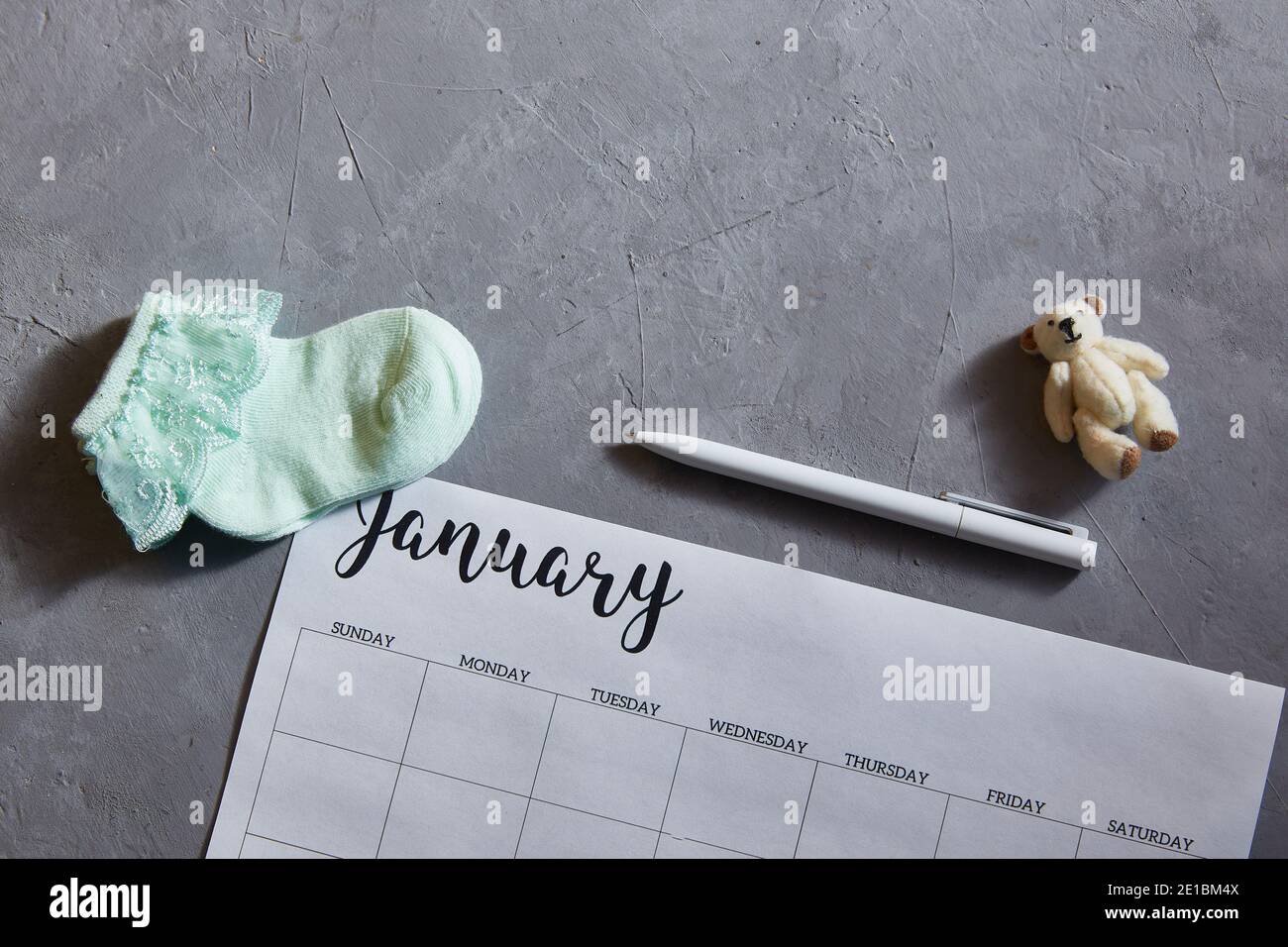 The announcement of the pregnancy. Baby socks, toy, calendar on a gray concrete background. Stock Photo